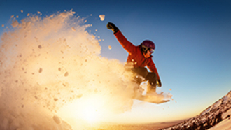 Action-Foto Snowboarder im Pulverschnee und Sonne im Hintergrund